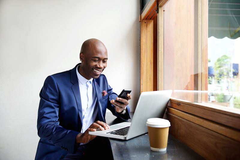 Happy African American man working on a laptop with a coffee in a cafe.